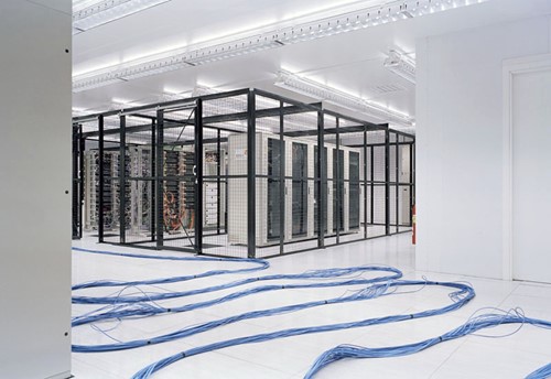 Bundles of blue cables run across the floor of a white room to a number of server racks