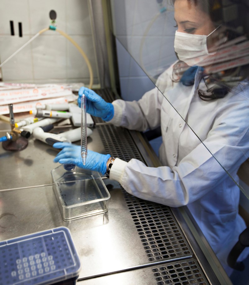 Woman in lab clothes wearing protective mask conducting tests in laboratory setting