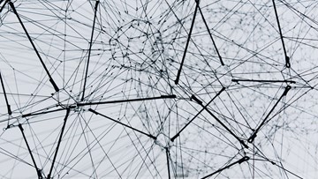 Black and white photograph of a complex web made of medal wires come in and out of various central nodes