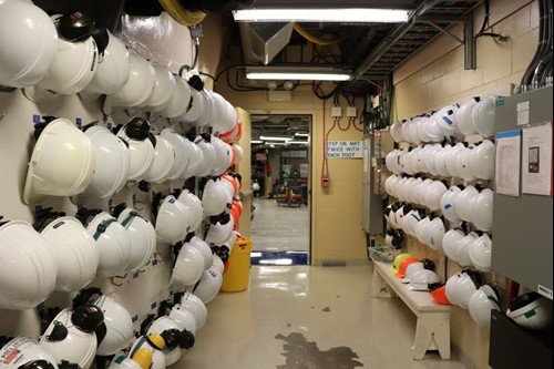 Racks of white hardhats in a hallway leading to open door looking out onto a laboratory