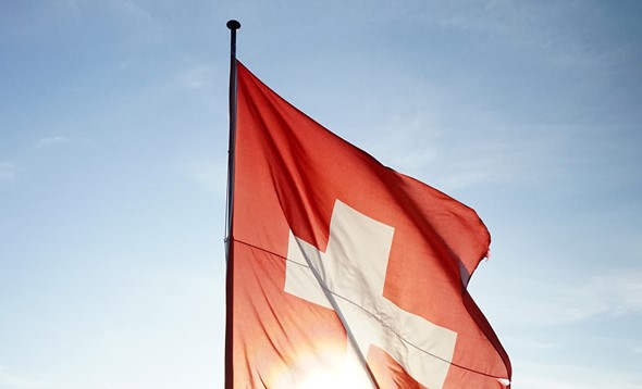 Swiss flag flying from a flag pole on a high vantage point looking out onto a valley and lake below