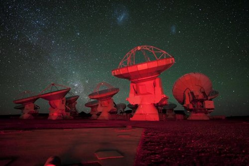 Dishes from the Atacama Large Millimeter Array illuminated in red light under a starry night sky
