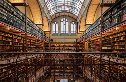 A classical multi-story library in a great hall, containing thousands of books