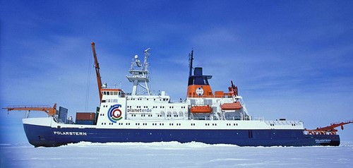 A blue-keeled research ship with a white top and red accents in sea ice