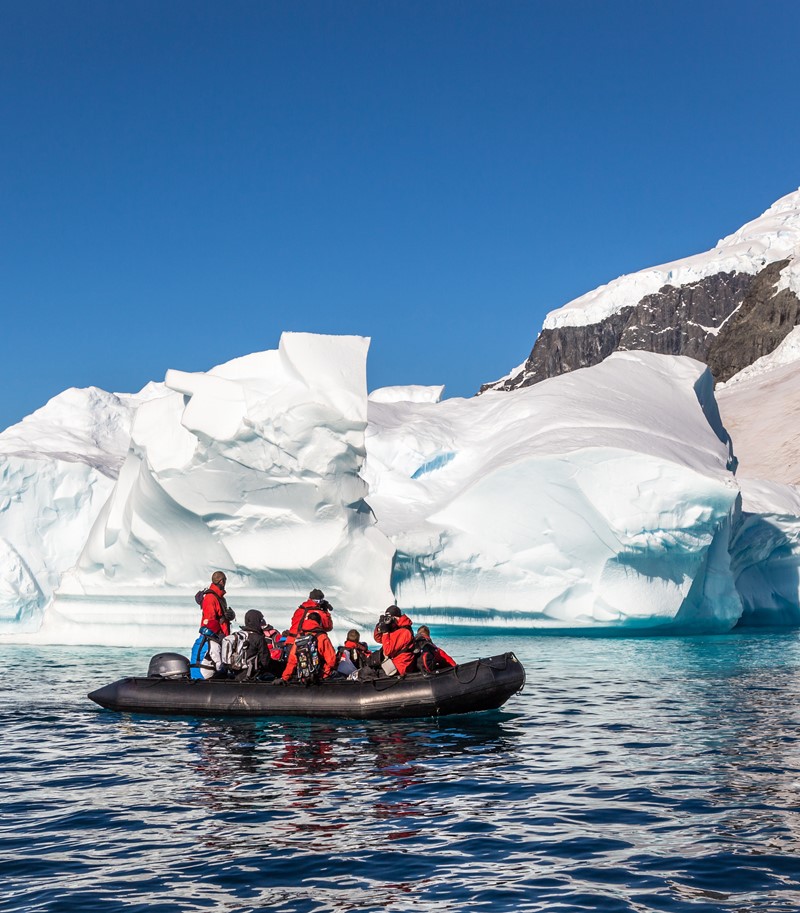 Several men in red jackets in a rubber boat passing in front of ice- and snow-covered rocks