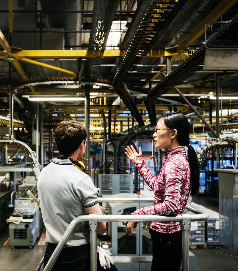 Profiled woman showing man with his back turned a large, industrial conveyor belt