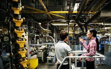 Profiled woman showing man with his back turned a large, industrial conveyor belt